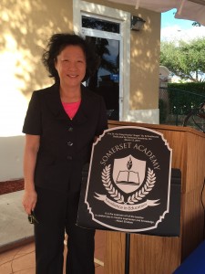 Angie Su in front of the new “Dr. Hui Fang Huang ‘Angie’ Su Schoolhouse”