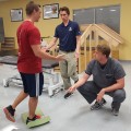 From left, a potential future PT student learns about and practices a balance test on foam at a Medical Career Day event, with help from second-year PT students Tim Marten and Brendan Bak.